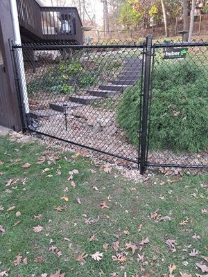 Black chain-link fence with gate in front of a green bush and steps leading uphill.