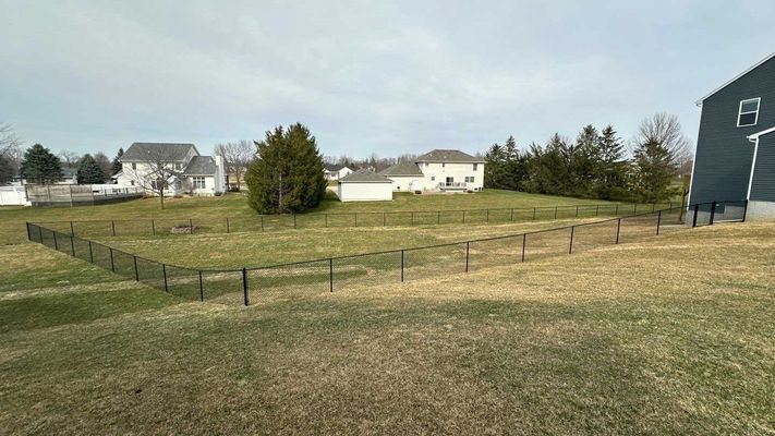 Black fenced-in backyard with surrounding homes on a cloudy day.