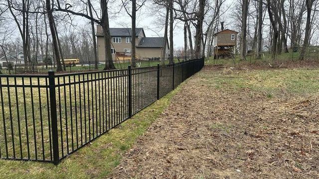 Black metal fence along a grassy hillside, with trees and a house in the background.