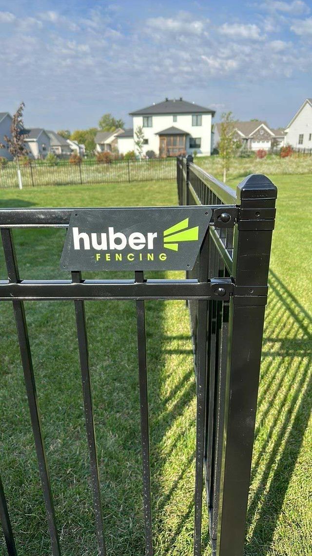 Black Huber fencing with logo, in a residential yard.