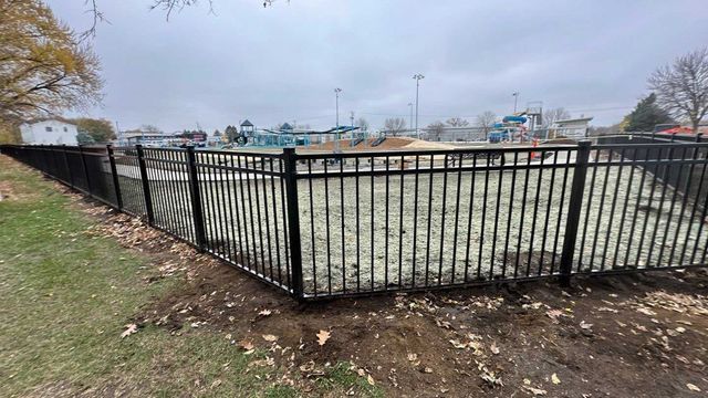 Black metal fence encloses an empty pool at an outdoor water park on a cloudy day.