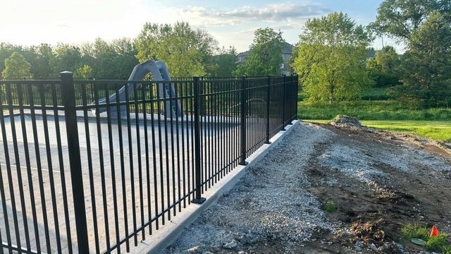 Black metal fence surrounding a concrete area; construction in progress.