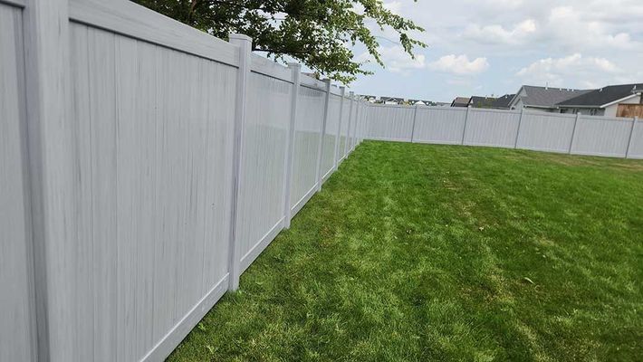 White vinyl fence enclosing a green lawn, under a cloudy sky.
