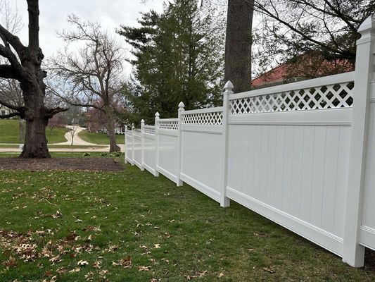 White vinyl fence on a grassy lawn, trees and road in the background.