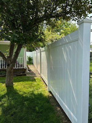 White vinyl fence along a yard, green grass, and a tree. Sunny day.