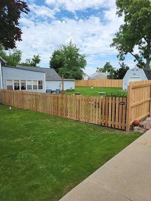 A wooden fence surrounds a green yard in front of a house and garage under a blue sky.