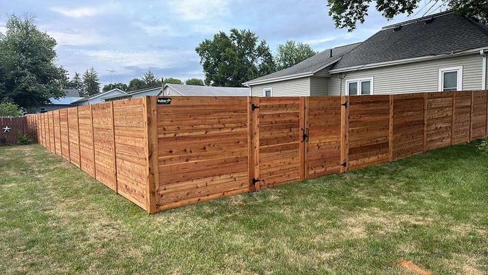 Wooden privacy fence encloses a yard with grass, a house, and a cloudy sky.