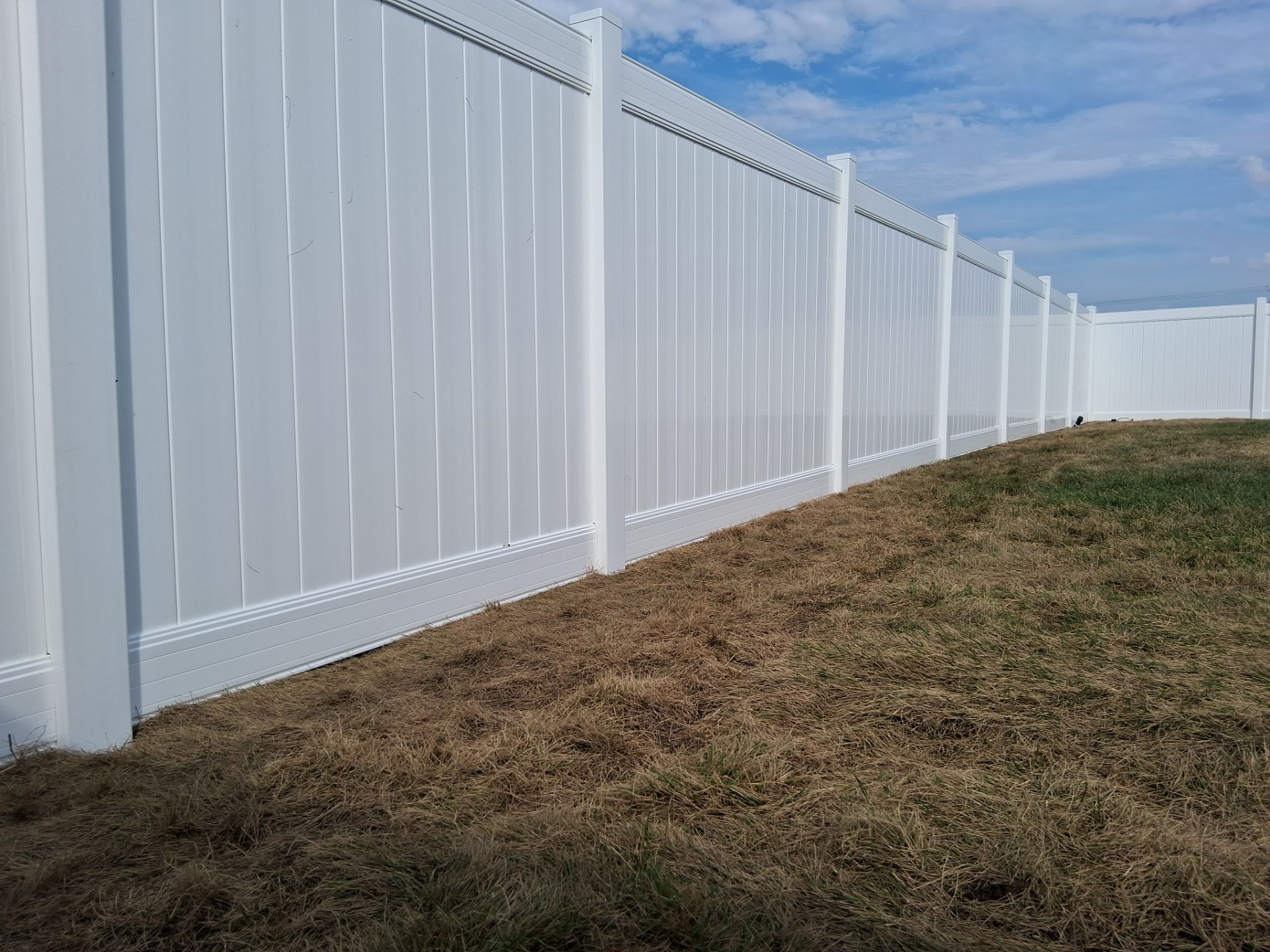 White vinyl fence along dry grass under a blue sky.