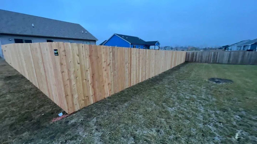 Wooden fence in a backyard under a cloudy sky. Grass in foreground, houses in the background.