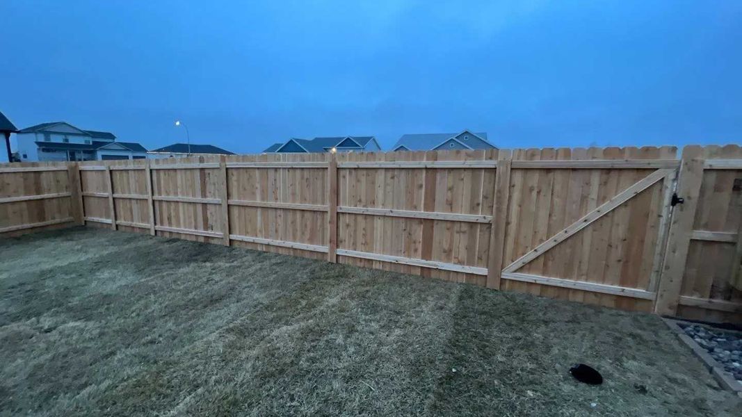 Wooden fence with gate in a grassy backyard under a cloudy sky.