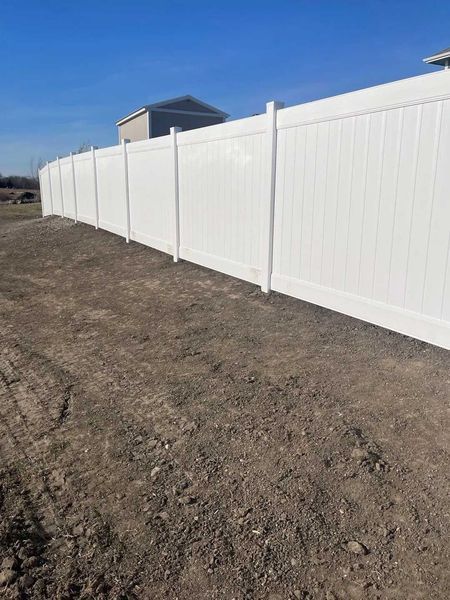 White vinyl fence on dirt under a clear blue sky.