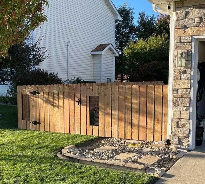 Wooden privacy fence with a gate, next to a house and garage, on a grassy lawn.