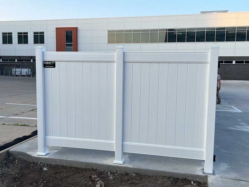 White vinyl fence in front of a building with a parking lot.