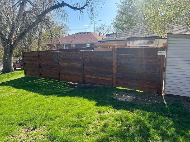 A dark wooden fence in a grassy yard, separating the lawn from neighboring houses.
