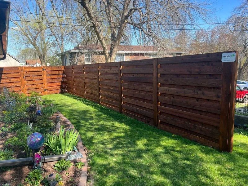 Brown horizontal slat fence along a green lawn in a sunny backyard.