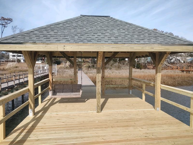 A wooden gazebo with a roof overlooking a body of water.