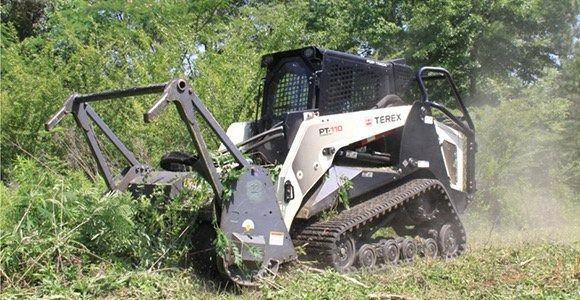 A track-mounted brush cutter clearing vegetation from a field.