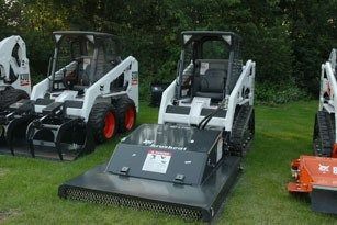 Skid steer loaders with different attachments sit on grass.