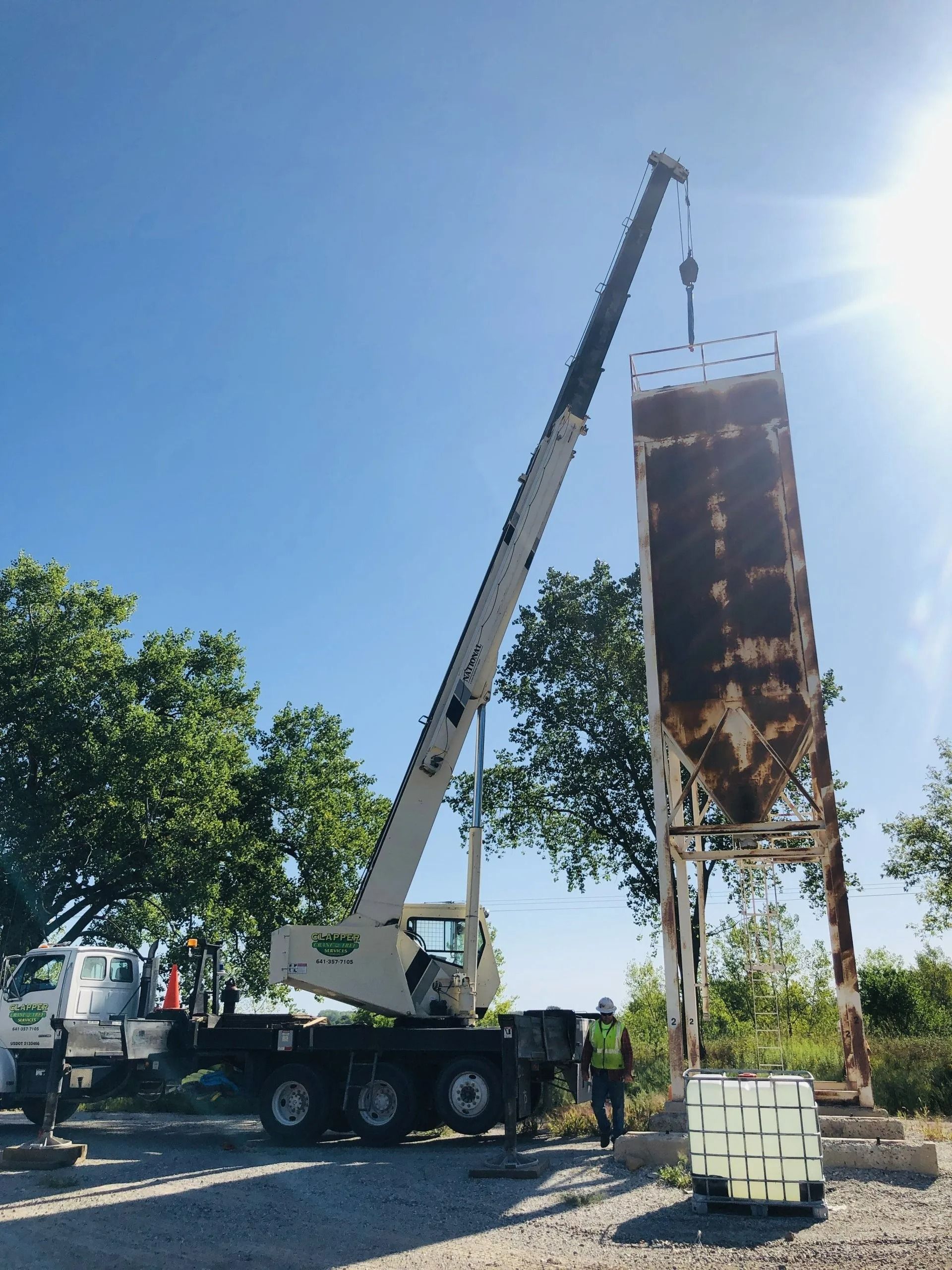 A crane lifting a rusty, tall silo structure on a sunny day.