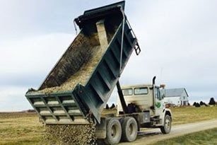Dump truck unloading gravel on a dirt road, rural landscape.