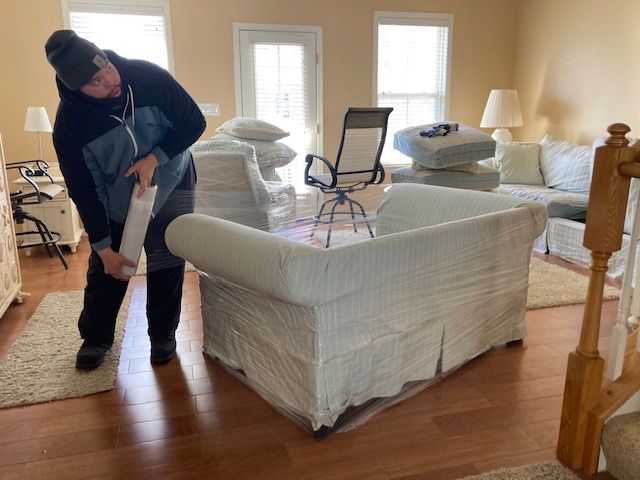 A man is wrapping a couch in plastic in a living room
