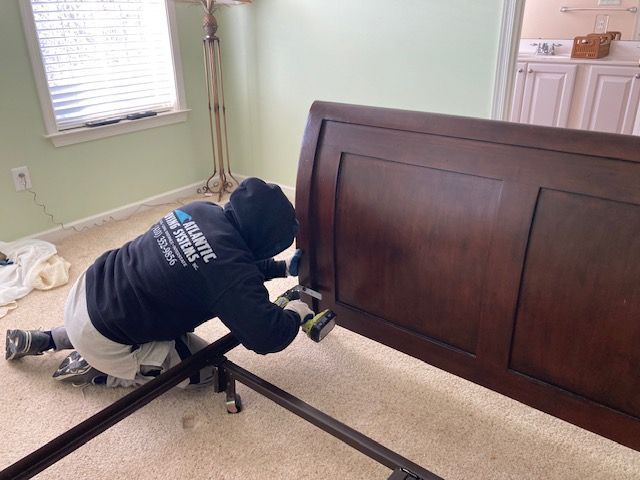 A man is working on a wooden bed frame in a bedroom.