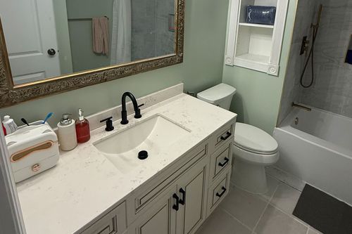 Bright bathroom vanity with white countertop, black faucet, mirror, toilet, and bathtub.