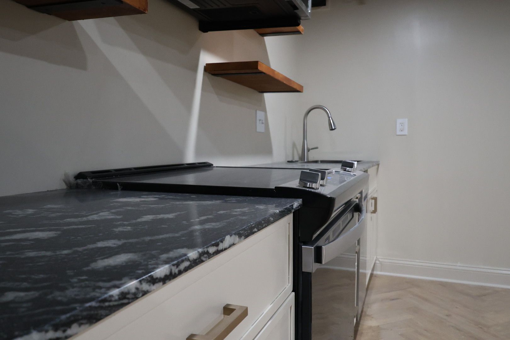 Modern kitchen with black countertops, floating shelves, sink, and stainless steel stove.