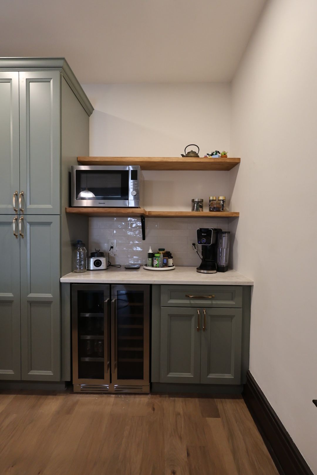 Kitchen corner with gray cabinets, wooden shelves, microwave, coffee maker, and wine fridge.