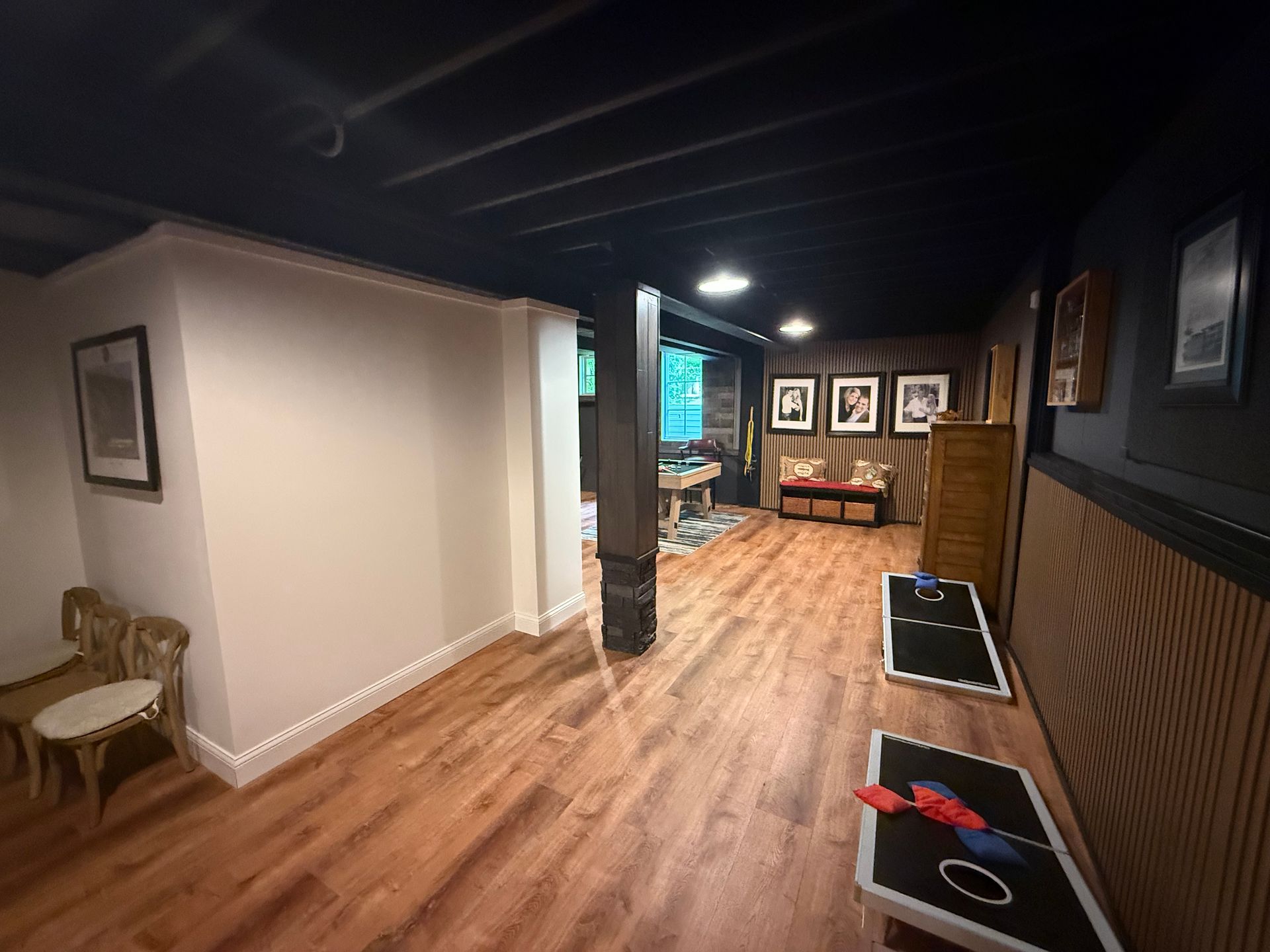 Modern hallway with wood floors, dark walls, framed art, and two black chairs with red accents