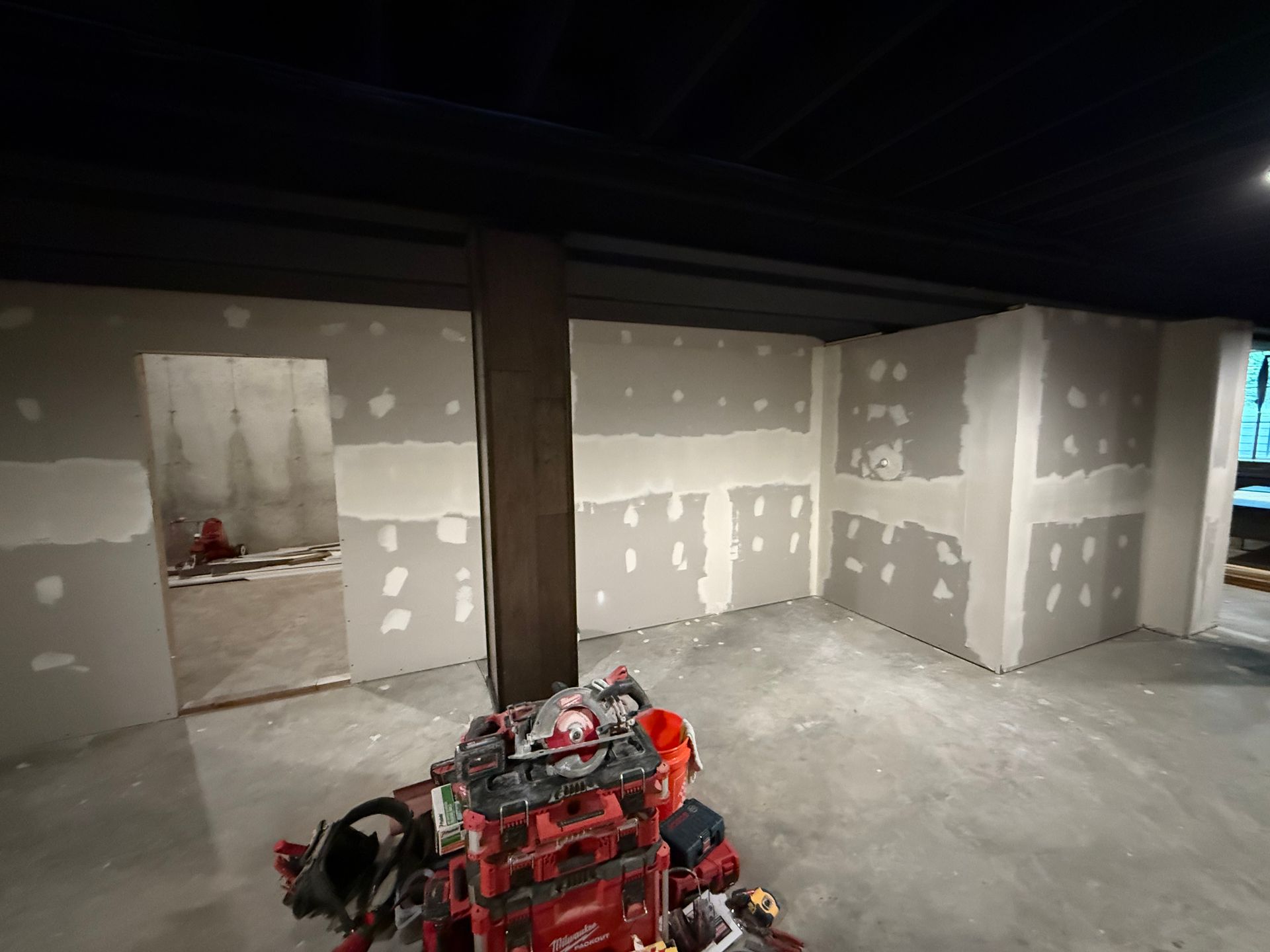 Unfinished interior with drywall walls and a red construction machine in the foreground