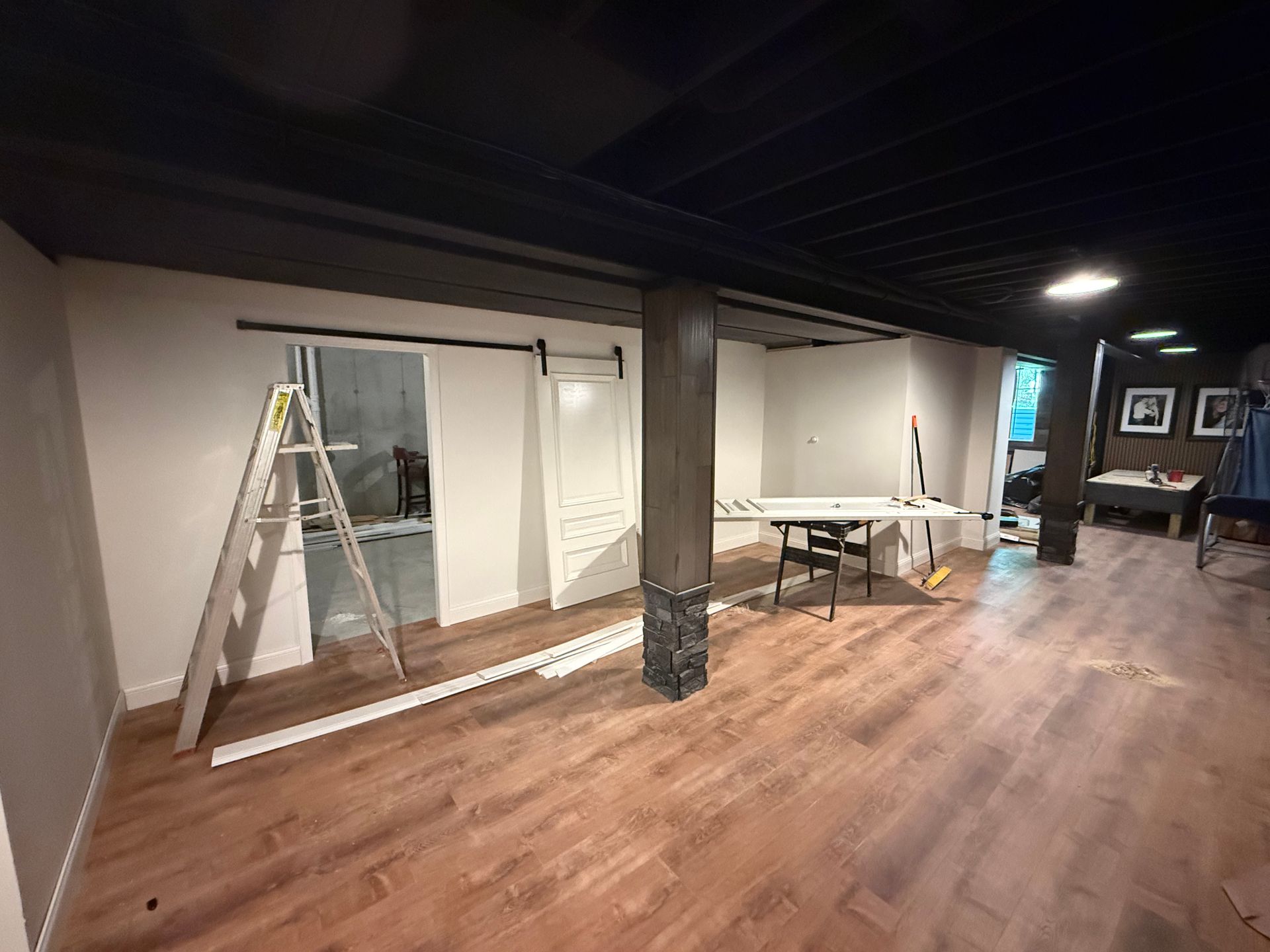 Empty basement room with wood floor, exposed ceiling, and a ladder near a wall under renovation