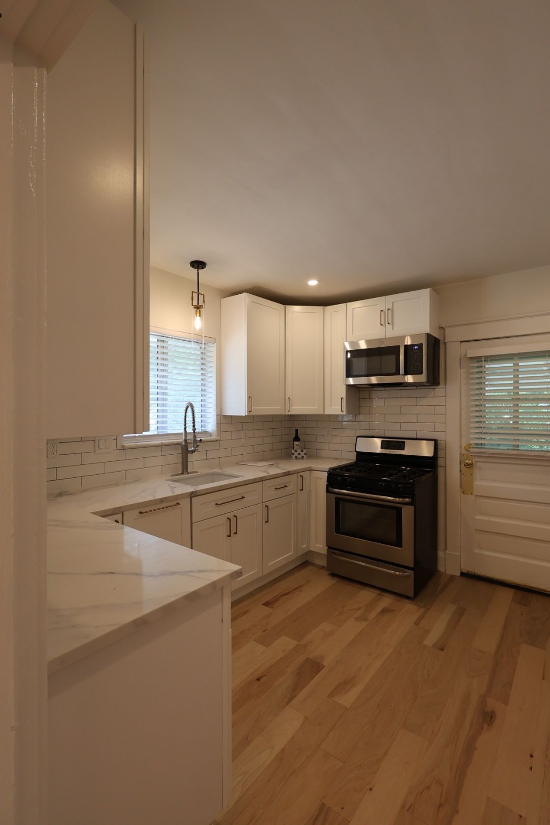 Bright kitchen with white cabinets, stainless steel appliances, wood floors, and a window over the sink.