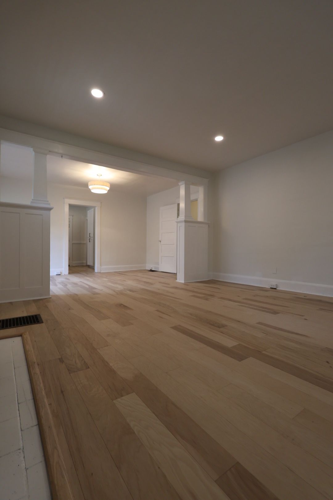 Empty modern living room with light wood floors, white walls, and recessed ceiling lights