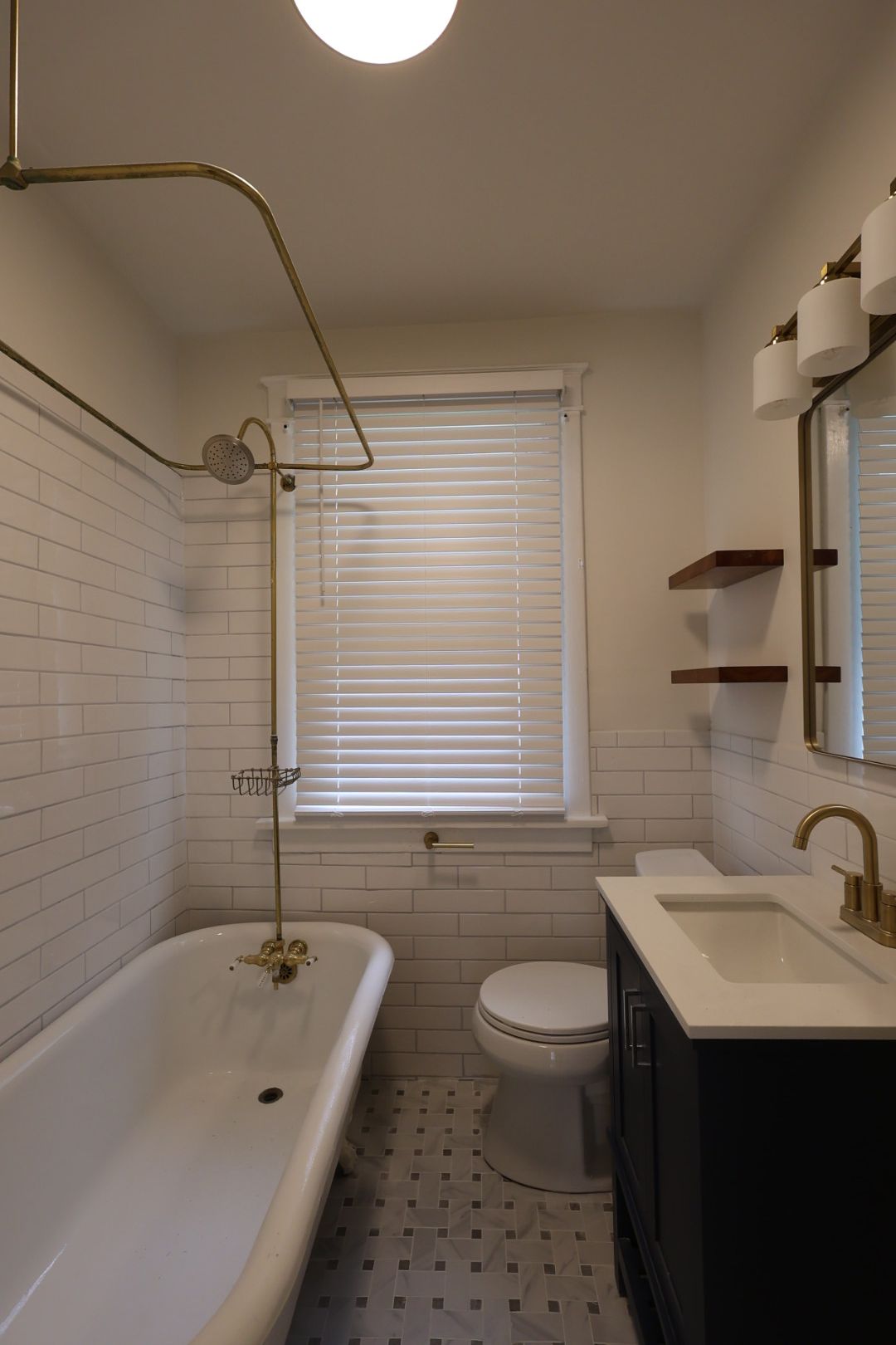 Bright white bathroom with clawfoot tub, sink vanity, toilet, window blinds, and gold fixtures.