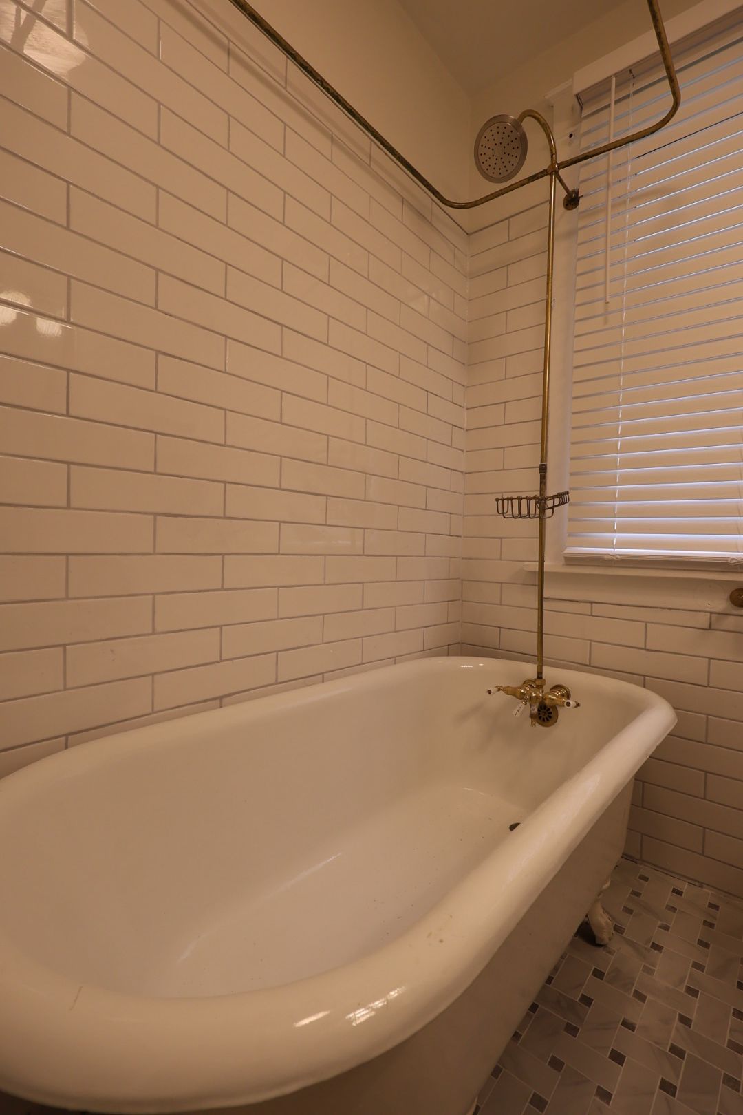 White clawfoot bathtub in a tiled bathroom with a window and hanging plant.