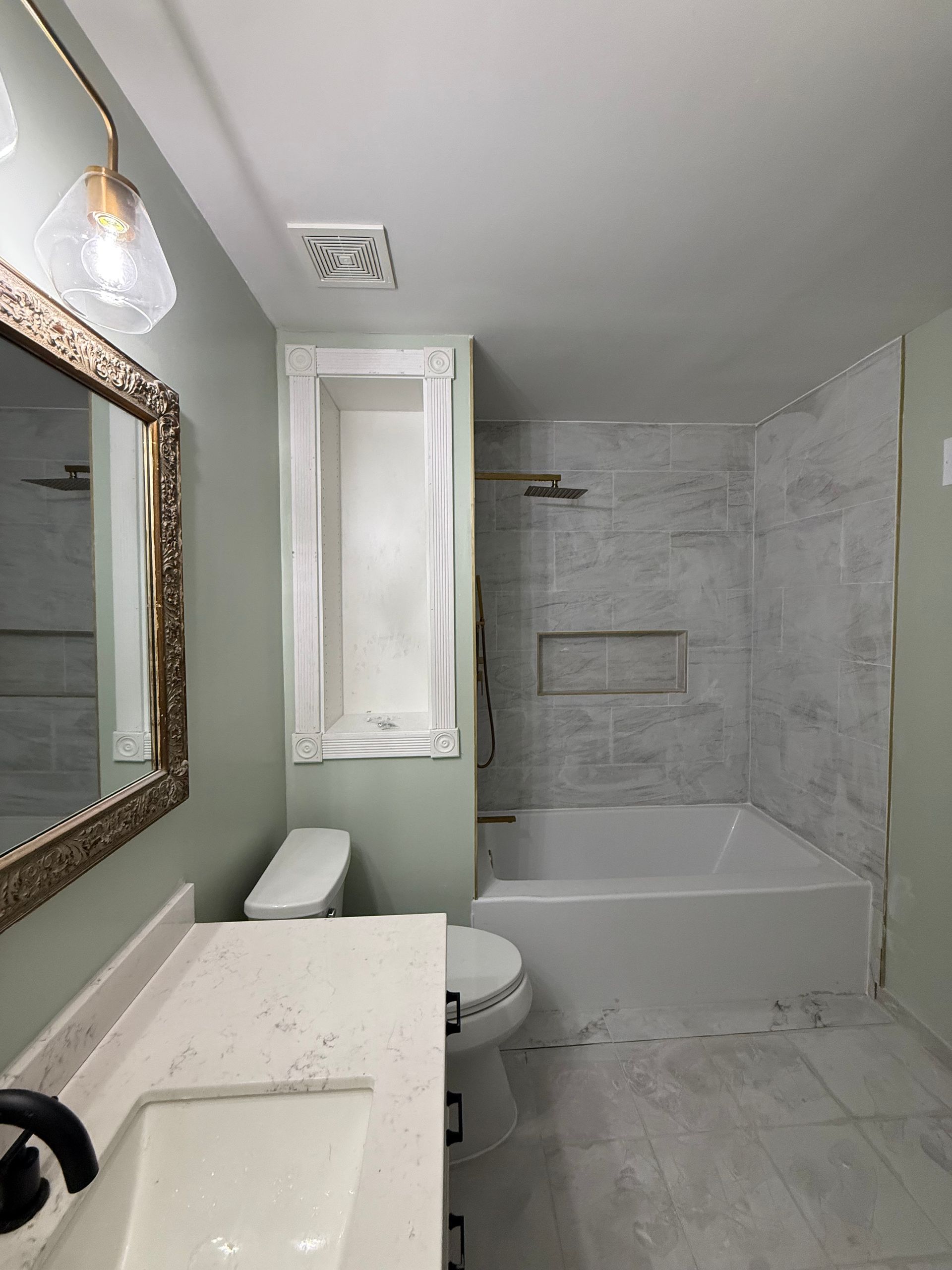 Small bathroom with marble tile, tub-shower, toilet, vanity, mirror, and window.