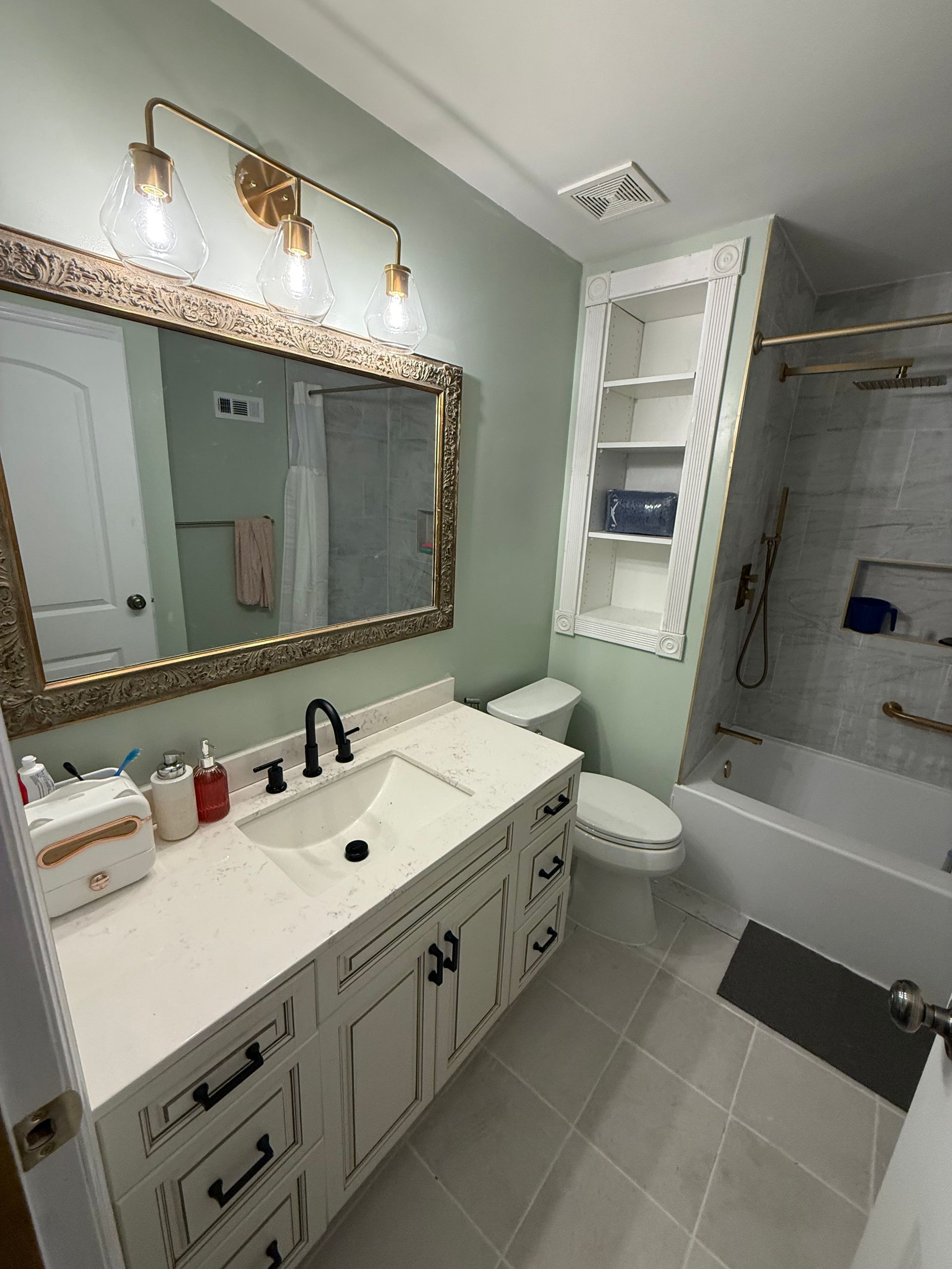 Bright white bathroom with vanity, mirror lights, toilet, tub, and gray tile floor