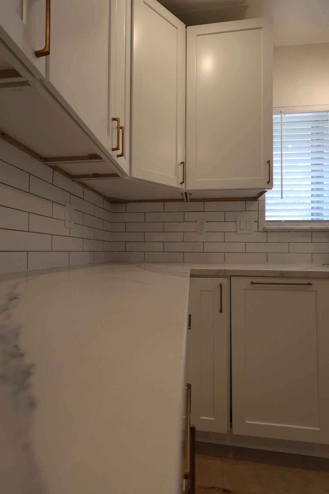 White kitchen with subway tile backsplash, beige cabinets, and a window with blinds.