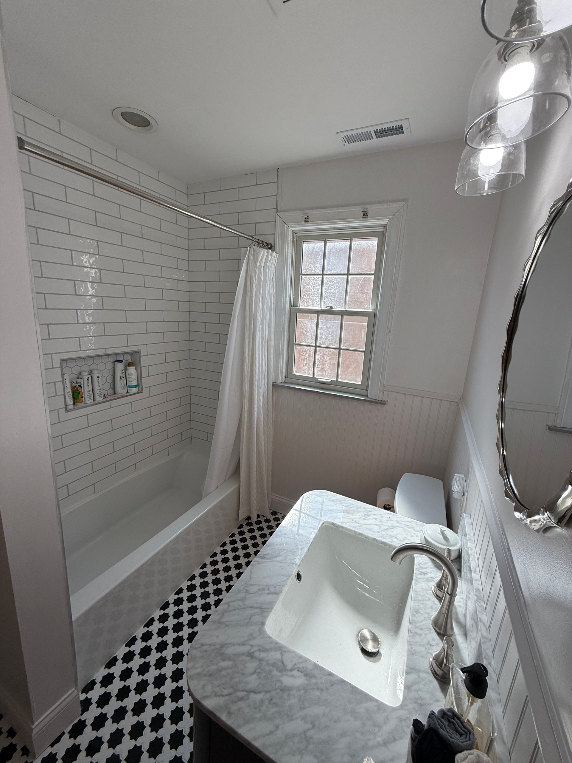 Bright white bathroom with subway tile, black-and-white floor, clawfoot tub, vanity, and window