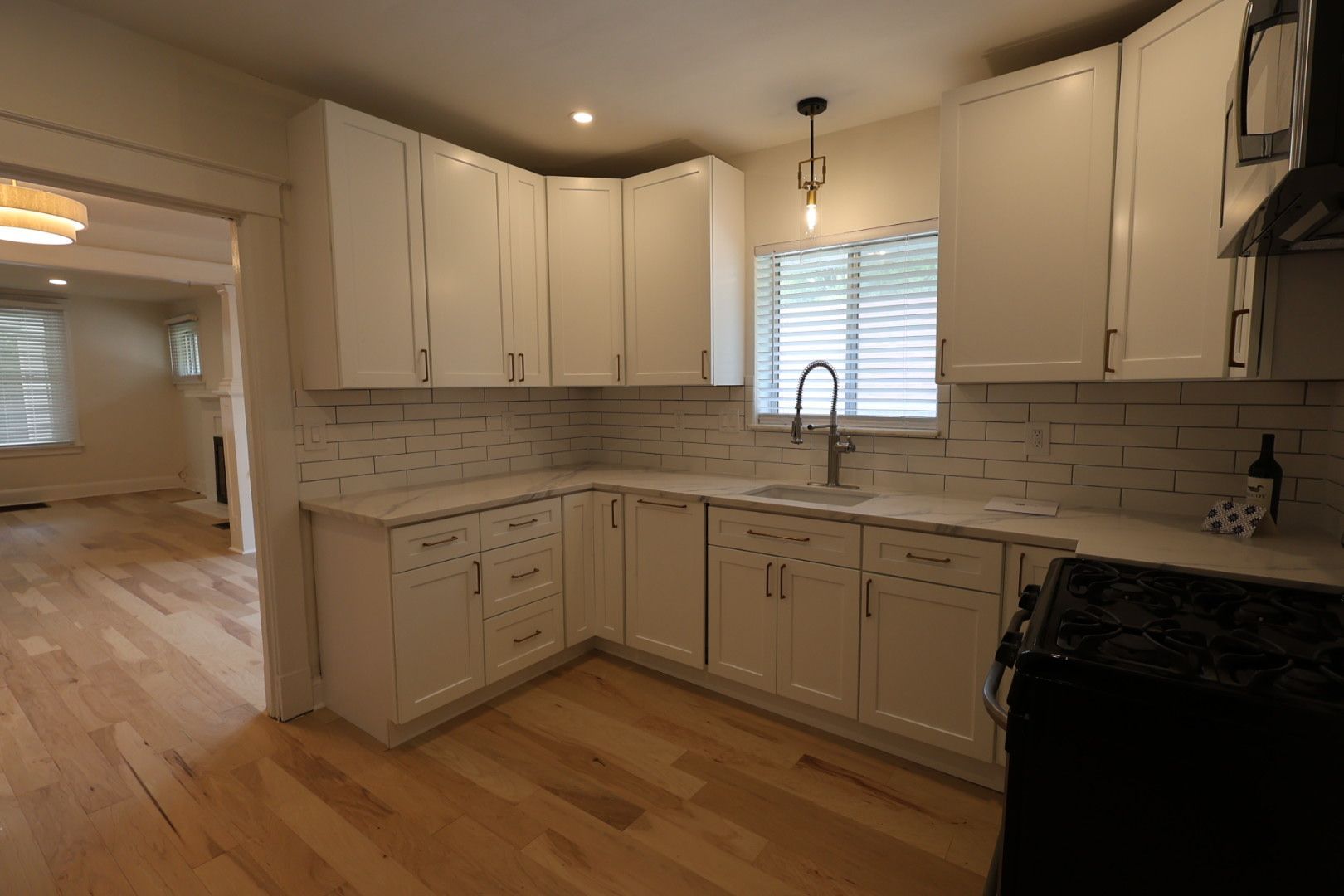 Bright kitchen with white cabinets, gray tile backsplash, wood floors, and a window over the sink.
