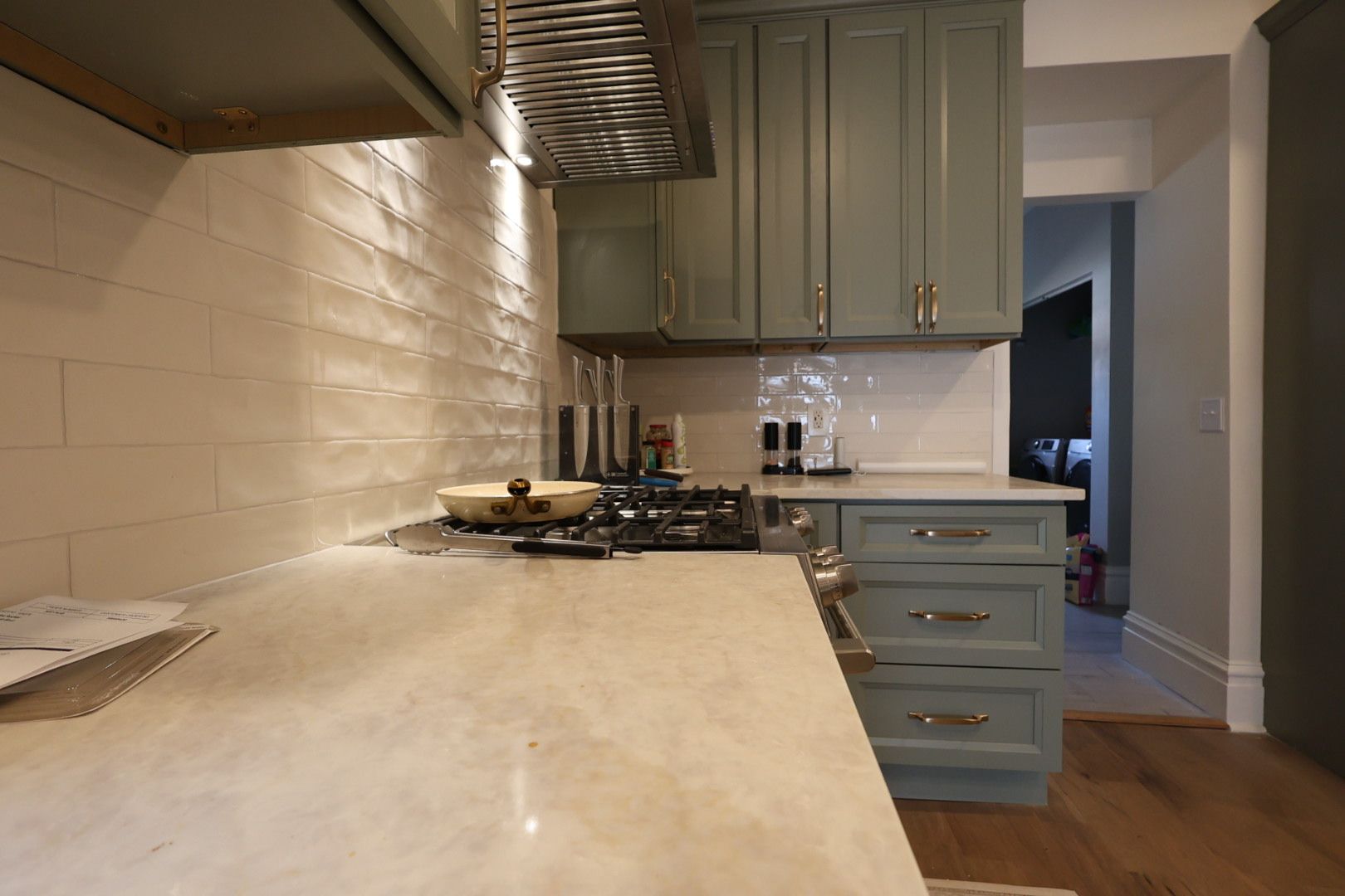 Kitchen countertop and gas stove with pale cabinets, white tile backsplash, and hardwood floor