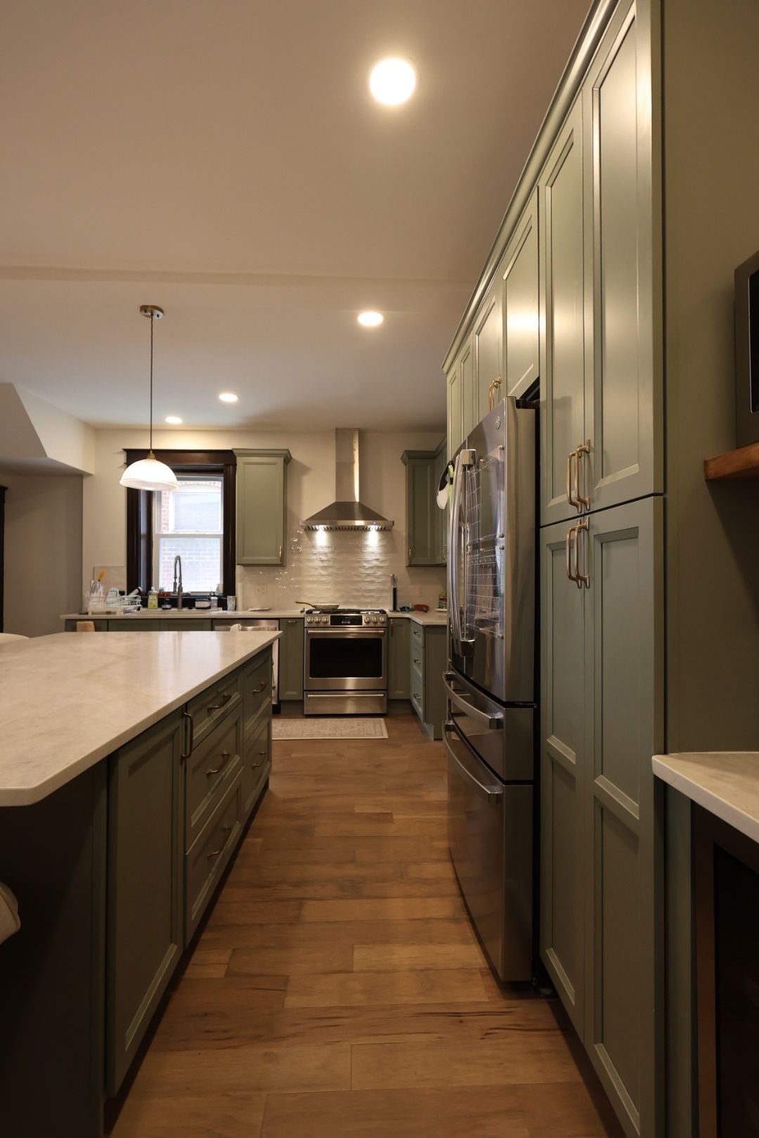Modern kitchen with wood floors, white island, stainless steel appliances, and recessed ceiling lights