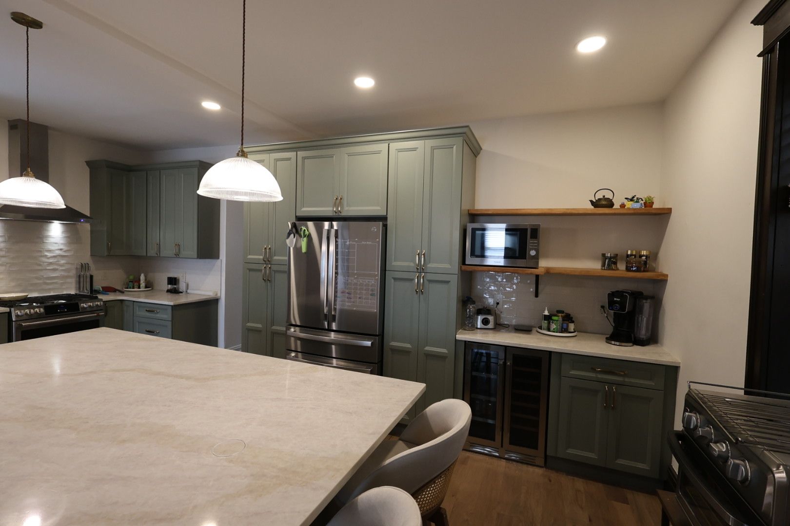 Modern kitchen with sage cabinets, stainless fridge, island, pendant lights, and open shelving