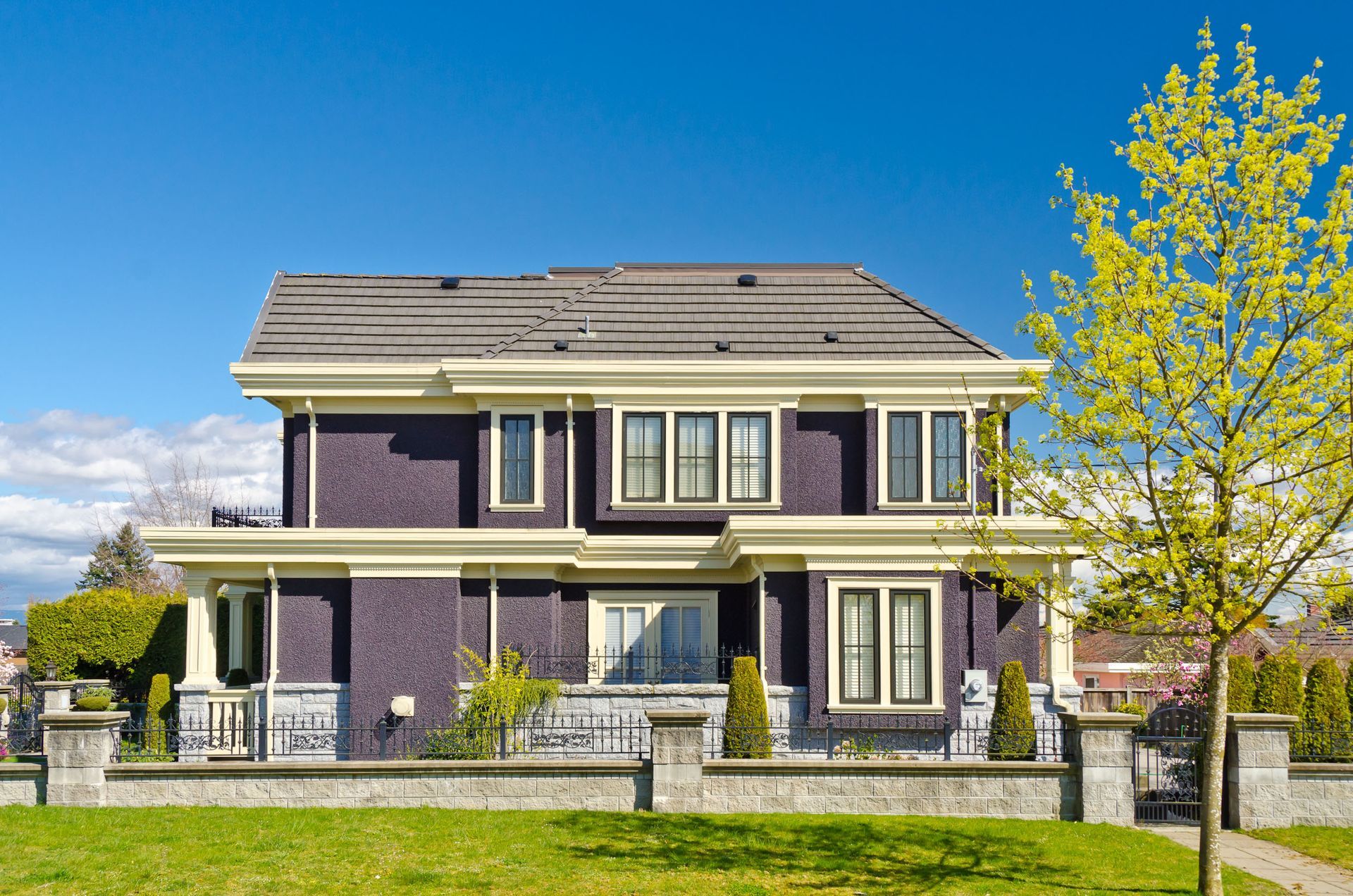 Purple two-story house with stone accents and a yellow-leaved tree under a bright blue sky