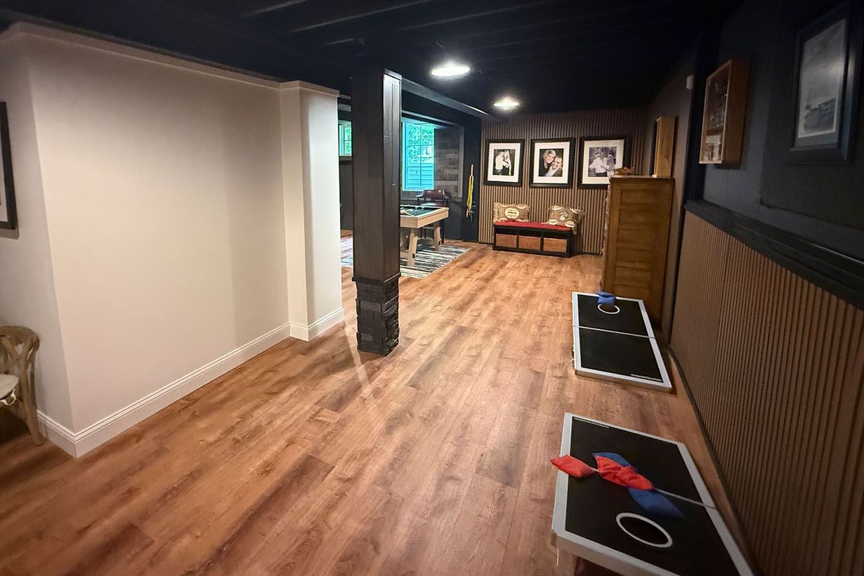 Dim hallway with wood floors, dark walls, framed photos, and small tables in a cozy interior space