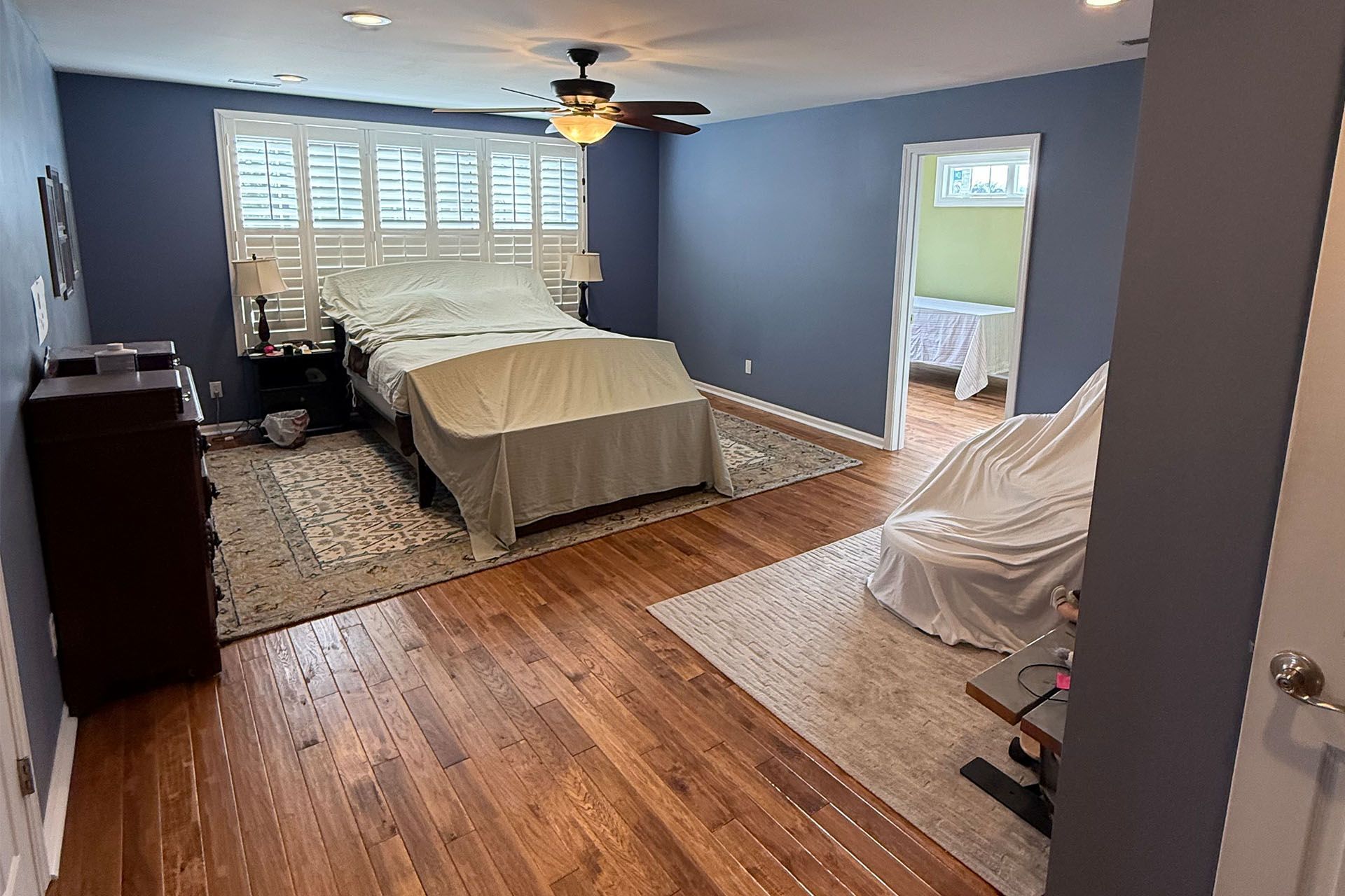 Bedroom with bed, hardwood floor, blue walls, and open doorway to a lit bathroom.