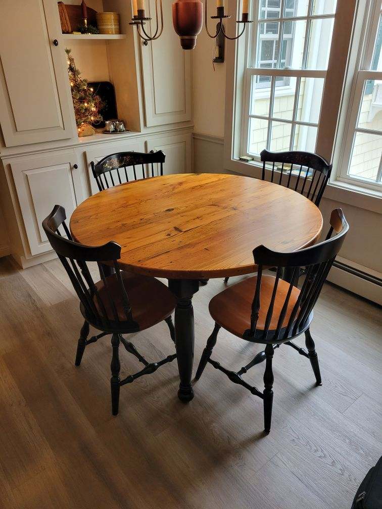 A round wooden table with four chairs in a room next to a window.