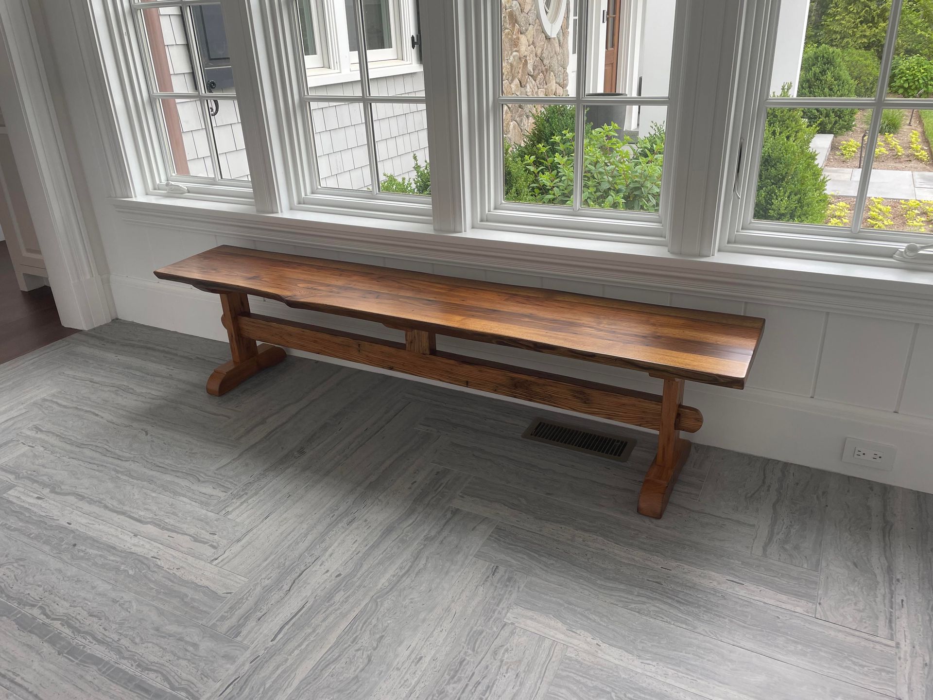 A wooden bench is sitting in front of a window in a room.
