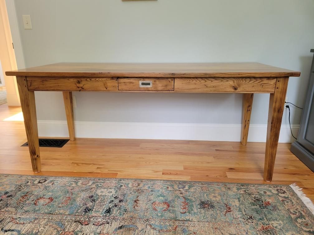 A wooden table is sitting on a wooden floor next to a rug.